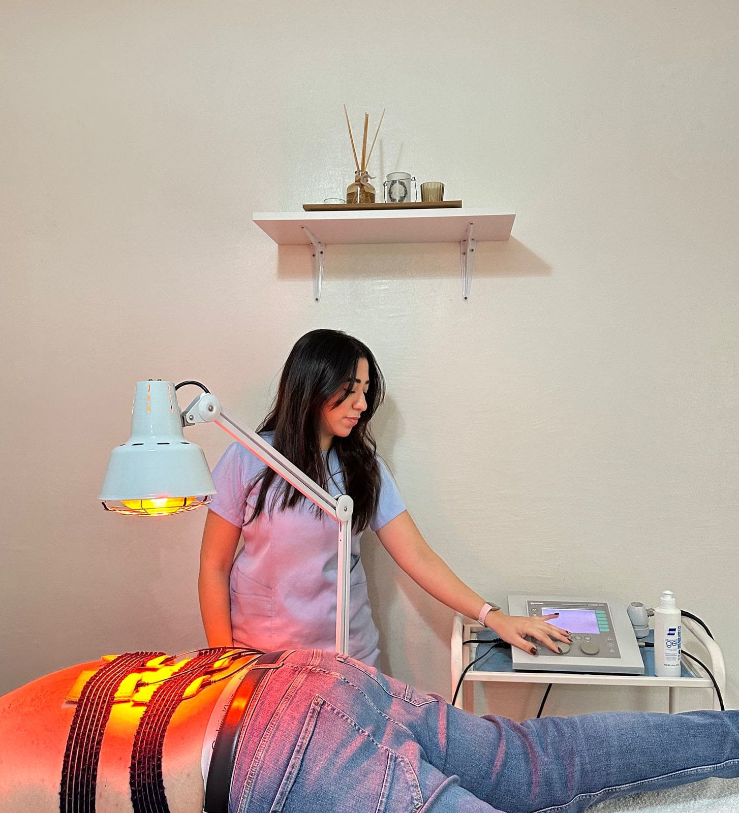 Kinésithérapeute réglant un appareil d'électrothérapie, patient sous lampe infrarouge