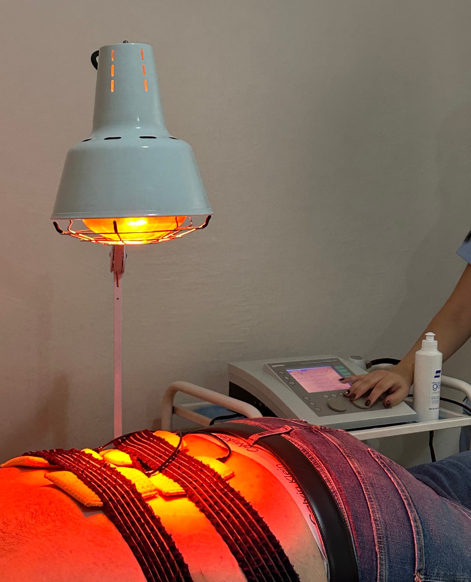 Électrodes d'électrothérapie posées sur le dos d'un patient, sous lampe infrarouge