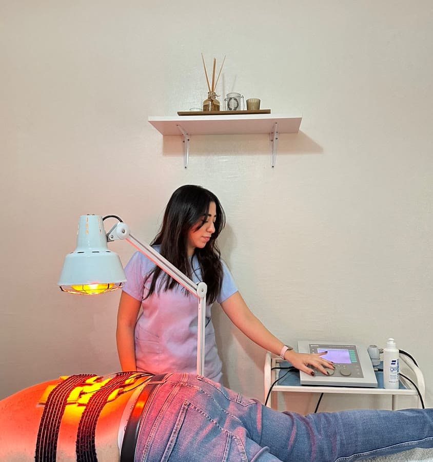 Kinésithérapeute réglant un appareil d'électrothérapie, patient sous lampe infrarouge